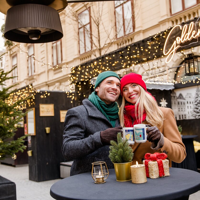 Advent in Graz I Winter in der Steiermark | © Graz Tourismus - Mias Photoart Paar in winterlicher Kleidung mit Tassen in der Hand vor festlicher Kulisse. | © Graz Tourismus - Mias Photoart